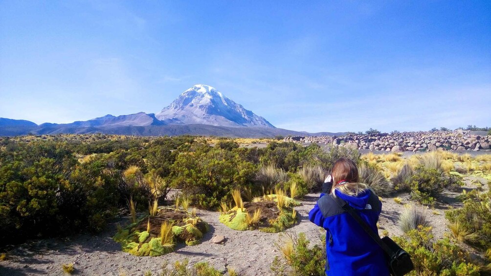 A person taking a photo of a snow-capped mountain with a rocky foreground. 1