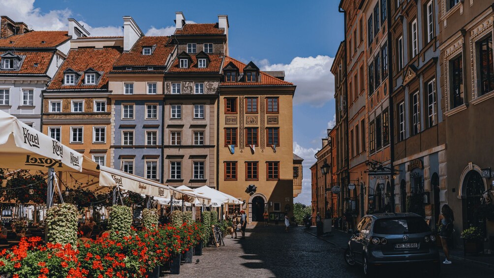 A cobblestone street lined with historic buildings and flower stalls. 1