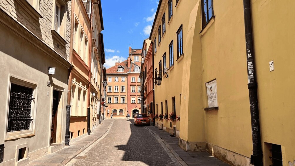 A cobblestone street lined with historic buildings, a red car parked on the right, and a clear blue sky. 3