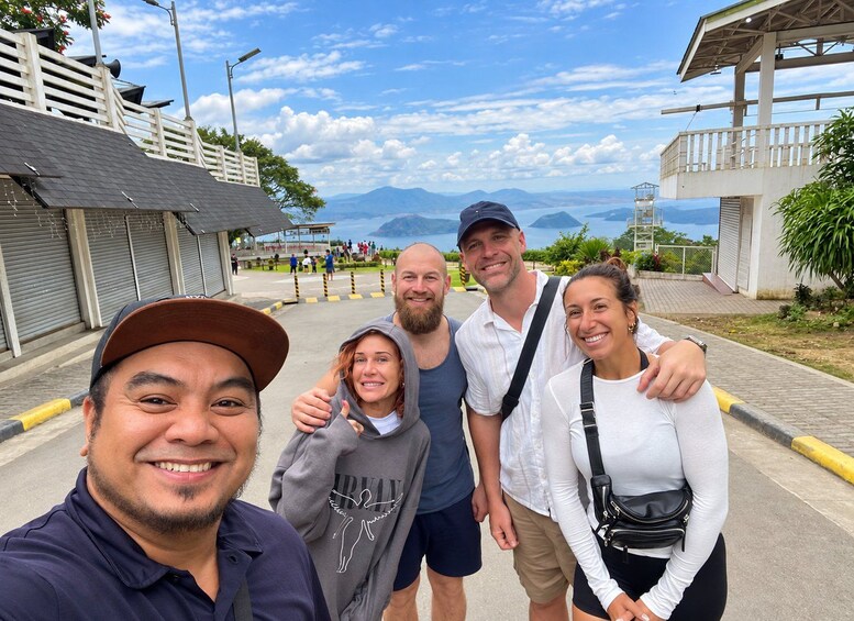 Un groupe de personnes prenant un selfie sur une promenade en bord de mer, avec la mer et les montagnes en arrière-plan. 5