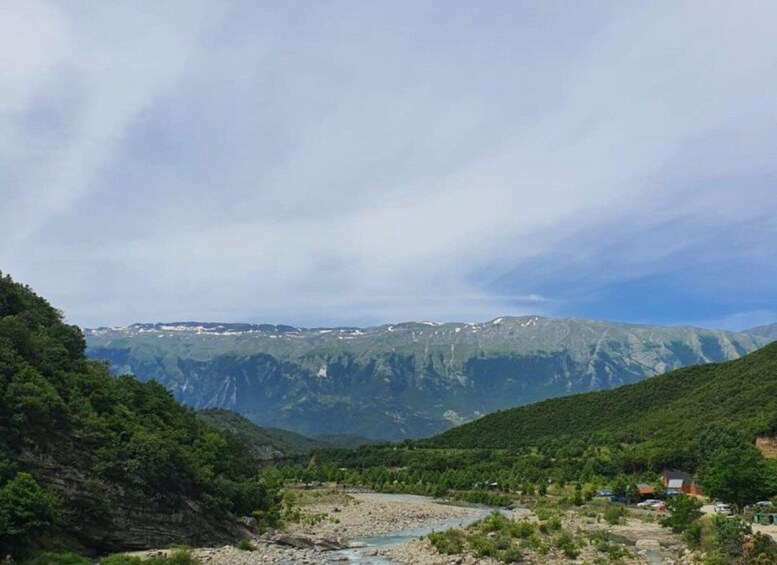 A river flowing through a valley with mountains in the background and a few houses on the right. 3