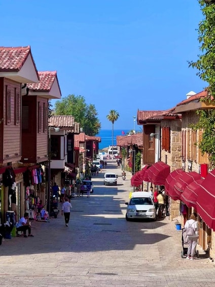 A narrow street lined with shops and red umbrellas, leading to a body of water. 1