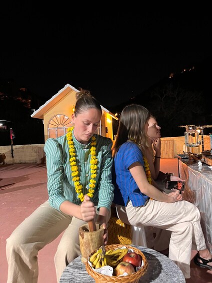Two people at an outdoor event, one pounding something with a wooden mallet, and a table with a basket of fruits. 1