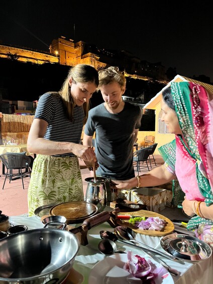 Three people cooking outdoors at night with a table full of cooking utensils and ingredients. 2