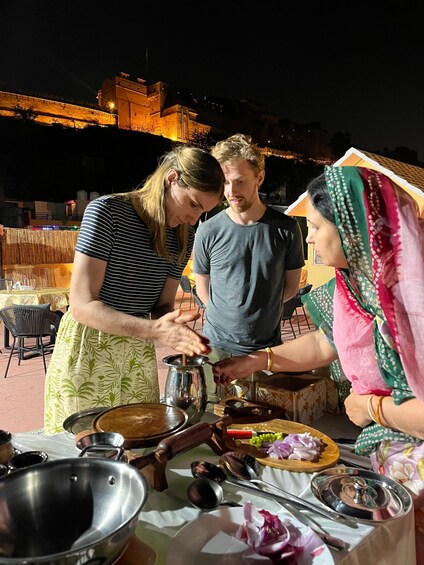 Three people preparing food outdoors at night with a table full of cooking utensils and ingredients. 1