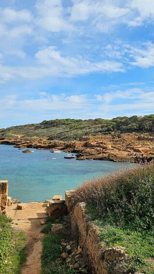 A coastal path leading to ancient ruins by the sea, with boats in the water and a clear sky. 1