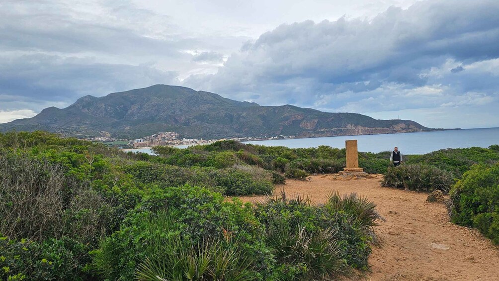 A coastal landscape with a path leading to a stone monument, a mountain in the background, and a body of water. 4