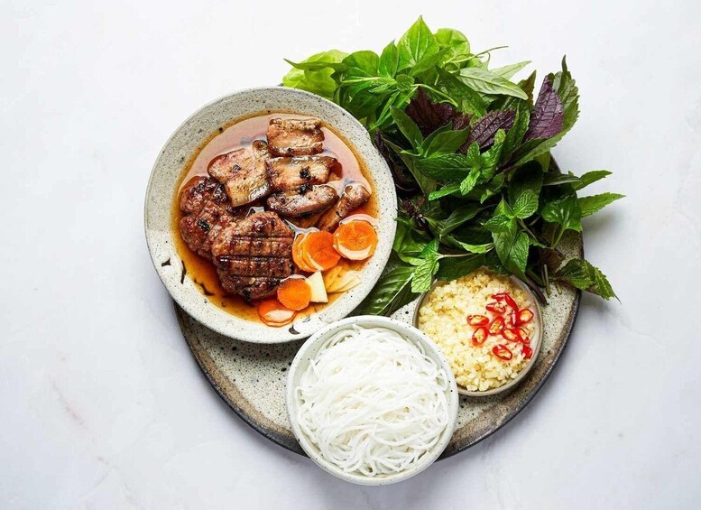 A bowl of beef with vegetables and noodles, accompanied by a side of rice and fresh herbs. 3