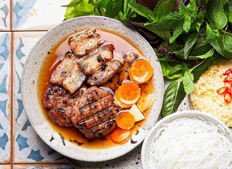 A bowl of grilled meat with vegetables and herbs, accompanied by a side of rice and noodles. 2