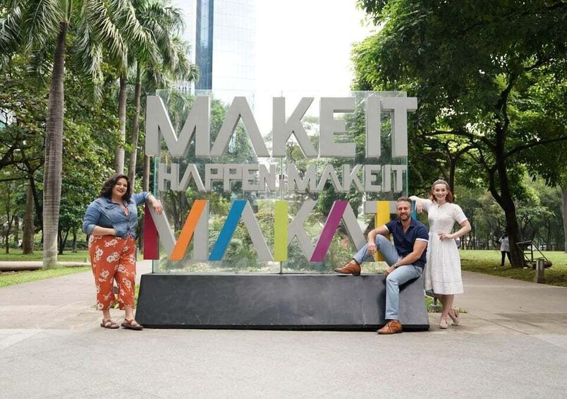 A group of people sitting and standing in front of a large, colorful sign with the text 'MAKE IT HAPPEN MAKE IT HAPPEN.' 5