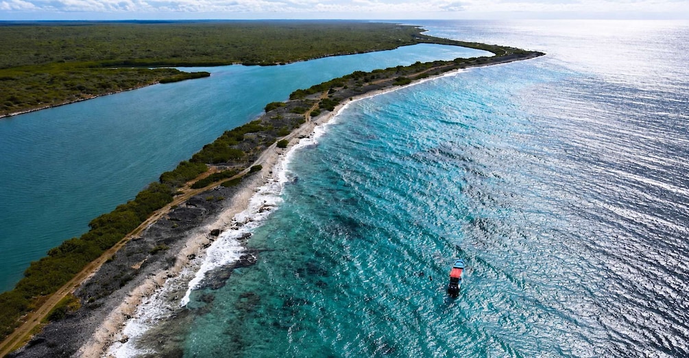 A coastal landscape with a clear blue sea, a sandy beach, and a road running parallel to the shore. 3