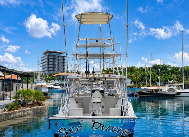 A blue boat named 'Sea Dust' docked at a marina with other boats and a building in the background. 1