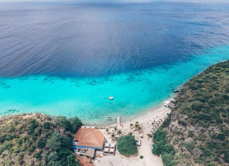 An aerial view of a beach with clear turquoise waters, a small boat, and a building with a red roof. 2