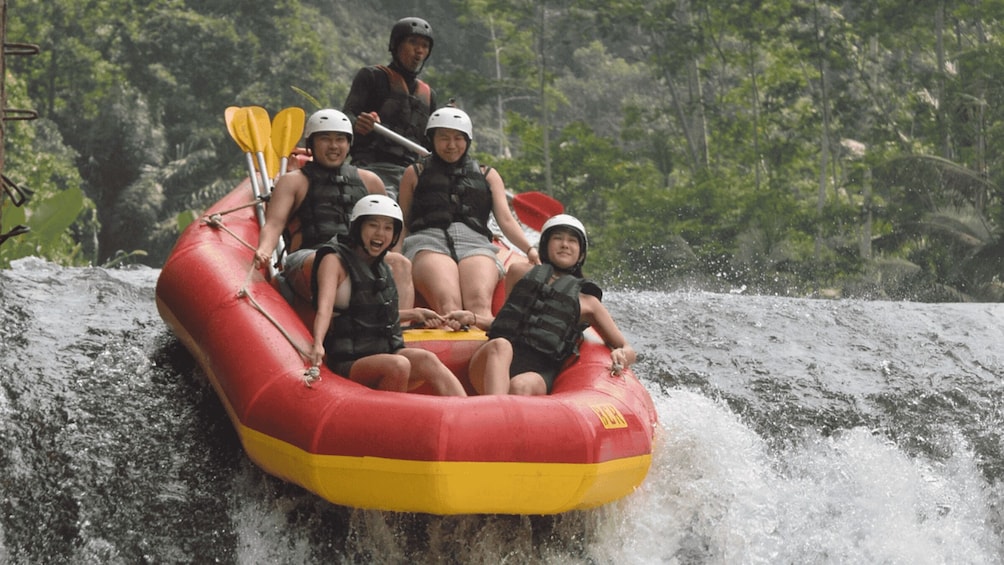 A group of people in a red and yellow inflatable raft navigating a waterfall. 5
