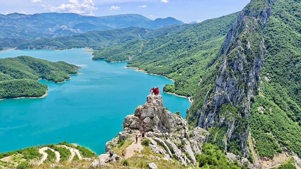 A mountainous landscape with a turquoise lake surrounded by lush greenery and rocky cliffs. 1