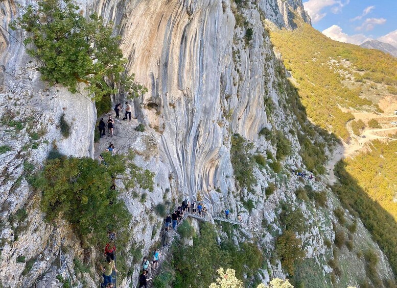 A group of hikers on a narrow, rocky mountain trail with steep cliffs and sparse vegetation. 4