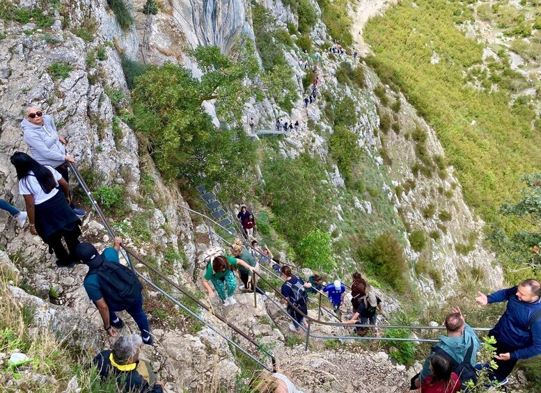 A group of hikers ascending a rocky mountain path with metal railings for support. 5