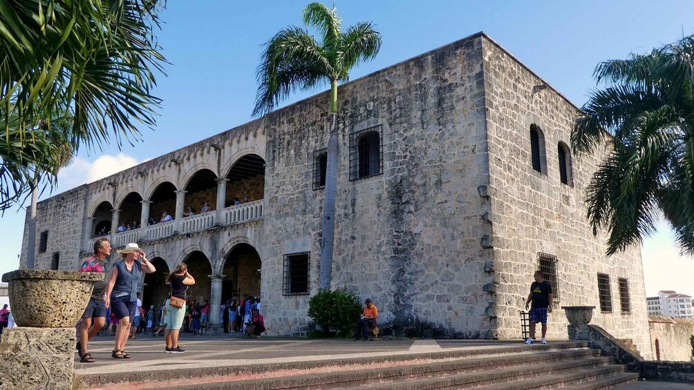 A historic stone building with arched windows and a palm tree in front. 5