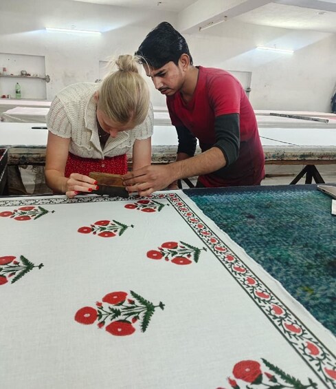 Two people working on a table with a tablecloth featuring red flowers and green leaves. 1