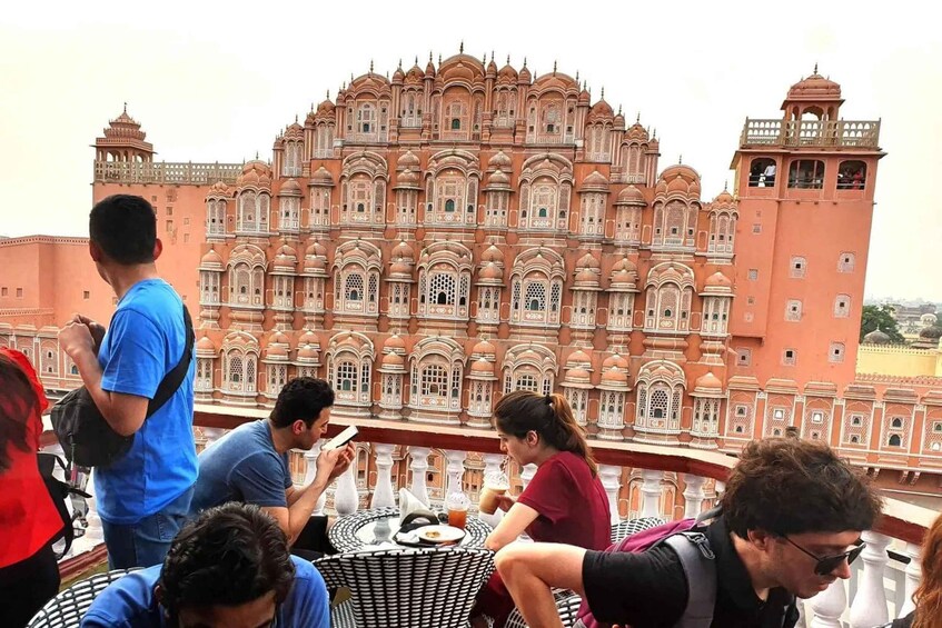 A group of people sitting on a terrace with a view of a large, ornate building. 1