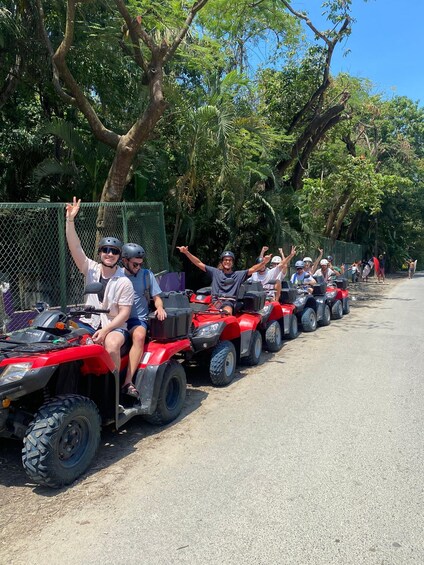 A group of people on ATVs lined up on a road with trees and a fence in the background. 3