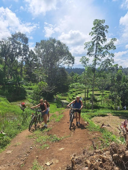 Two people on bicycles on a dirt path surrounded by lush greenery and trees. 5