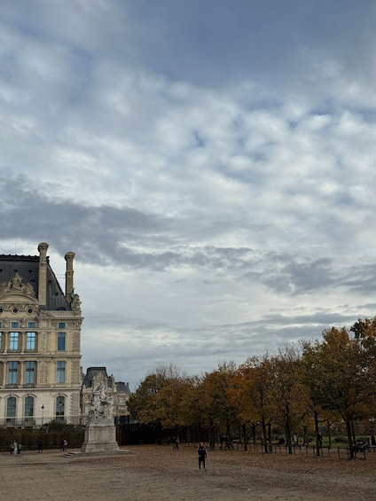 A historic building with classical architecture, a statue in the foreground, and trees with autumn leaves in a park. 5