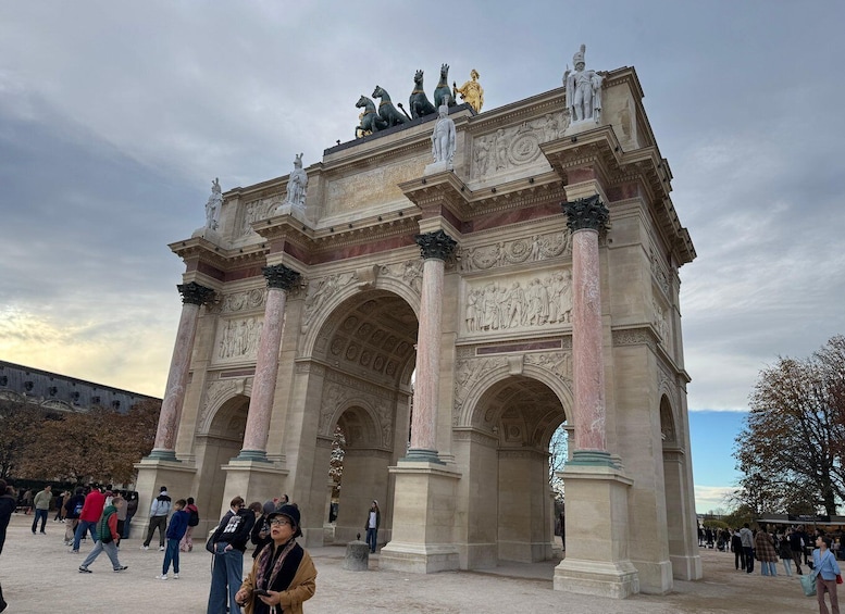 A large, ornate archway with sculptures and columns, surrounded by people. 1