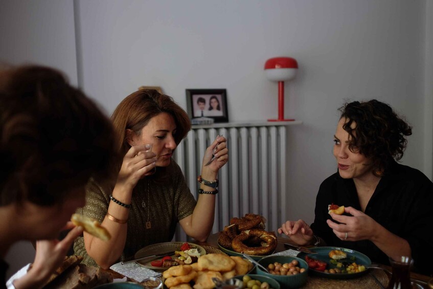 Three people sitting at a table with various foods, a framed photo on the wall, and a red lamp. 1
