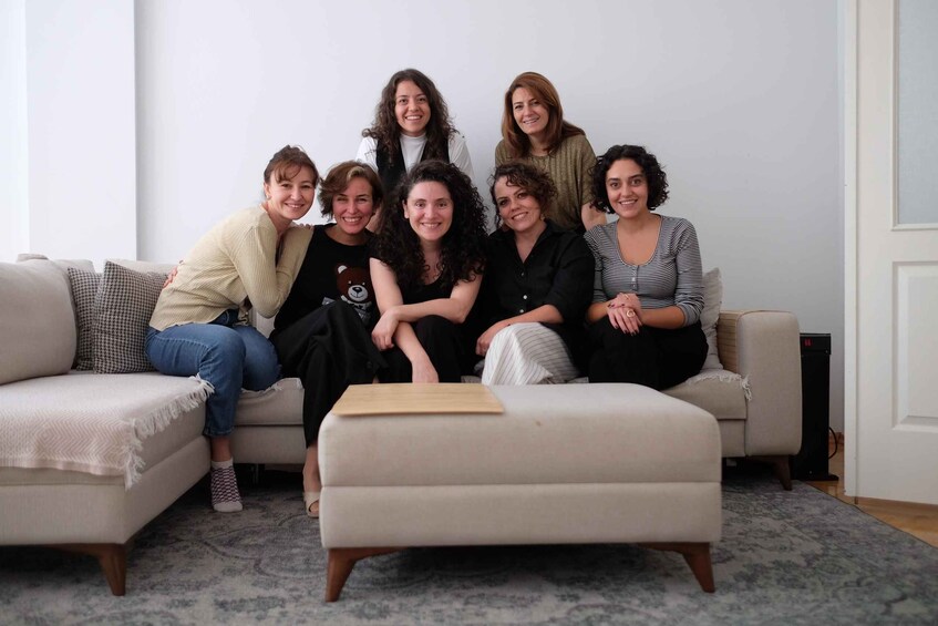 A group of people sitting on a couch in a living room with a patterned rug and a white door in the background. 5