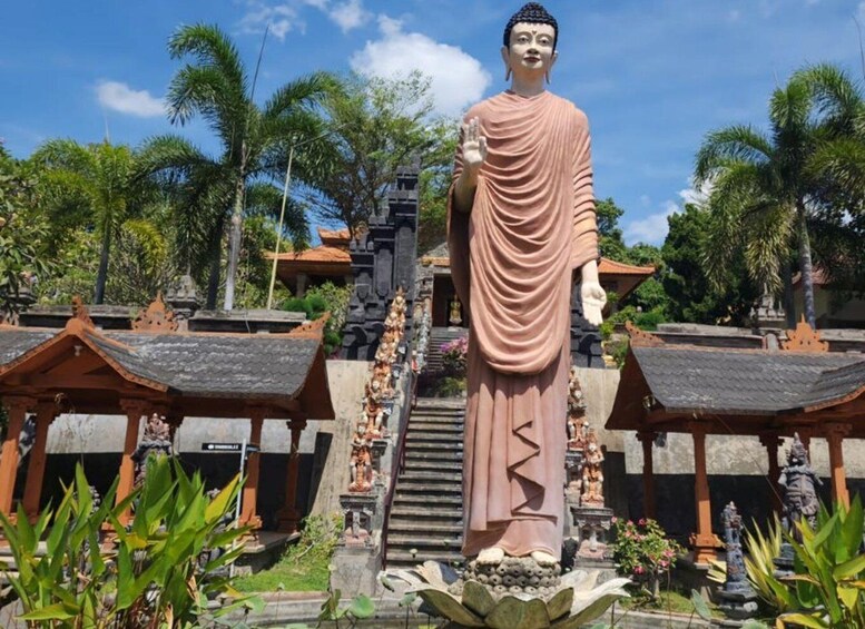 A large Buddha statue in a temple complex with traditional architecture and tropical surroundings. 5