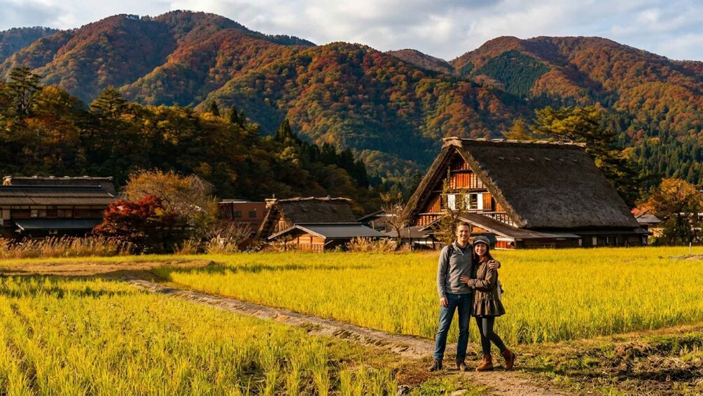 A couple standing in a rice field with traditional houses and mountains in the background. 5