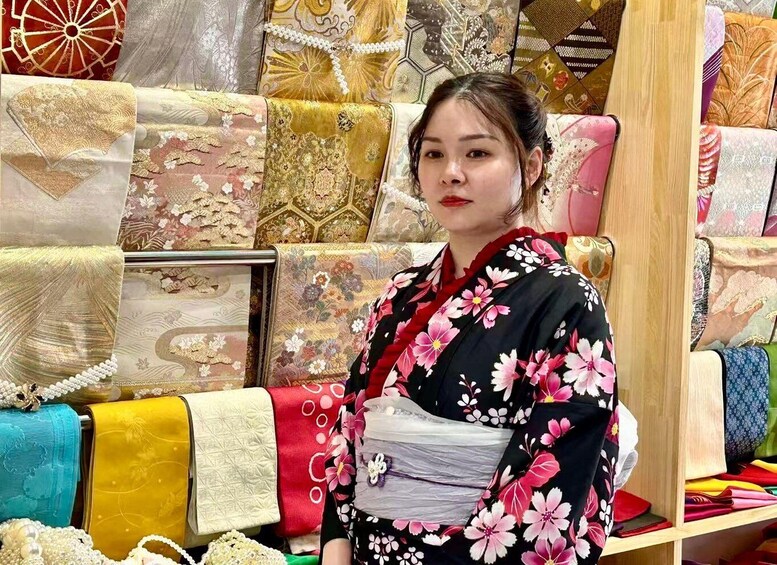 A person in a kimono with floral patterns standing in front of a display of various textiles. 3