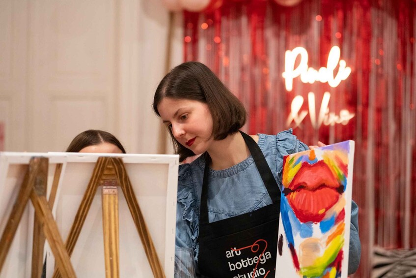 A person holding a colorful painting with a black apron that reads 'art bottega studio.' 1