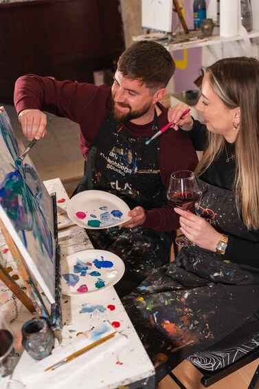 Two people painting at a studio with paint splatters and a wine glass. 3