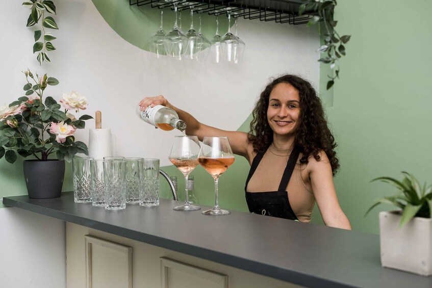 A person pouring a drink into a glass at a bar counter with potted plants and wine glasses. 4