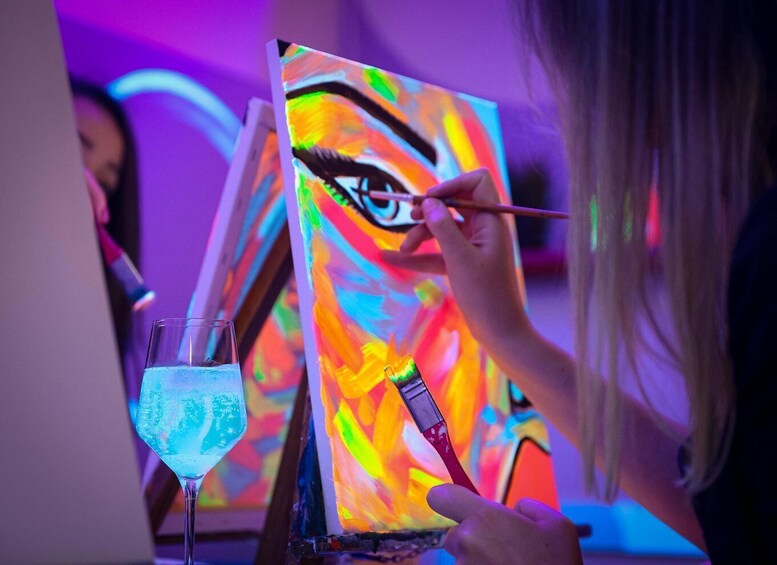 A person painting a vibrant abstract artwork with a colorful drink in a glass nearby. 5