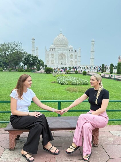 Två personer sitter på en bänk och tittar mot Taj Mahal. 2