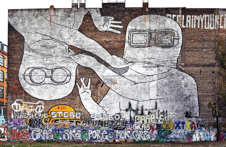 A mural with graffiti and a large figure holding glasses. 2