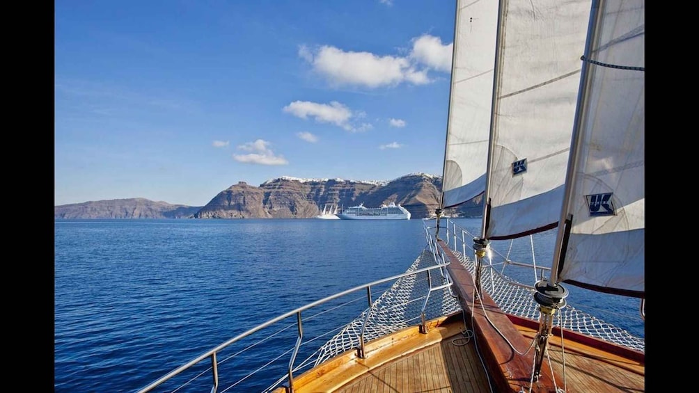 A sailboat with a view of a cruise ship and rocky cliffs in the distance. 1