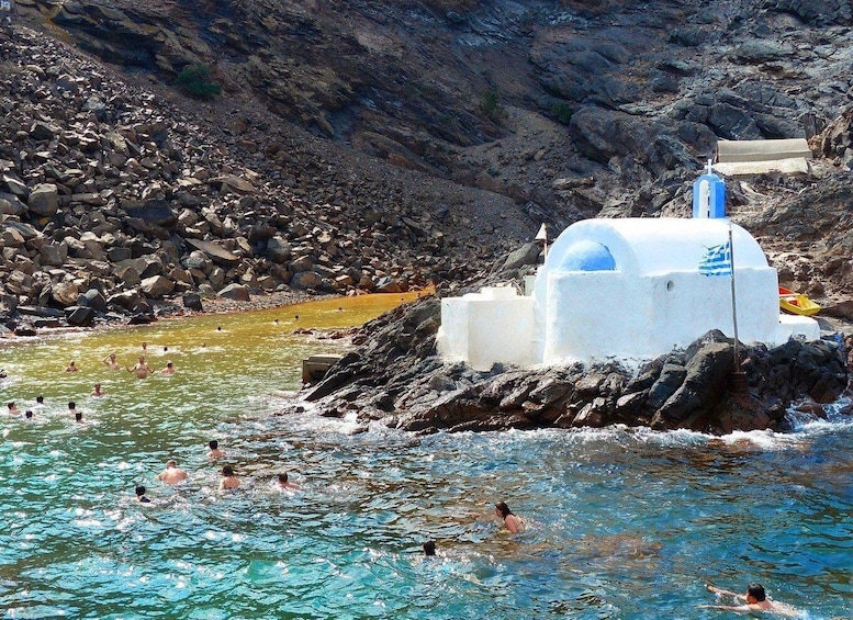 A rocky coastal area with a white building, possibly a lifeguard station, and people swimming in the water. 2