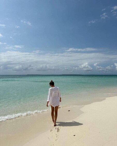 A person walking on a sandy beach with clear turquoise water and a clear sky. 2