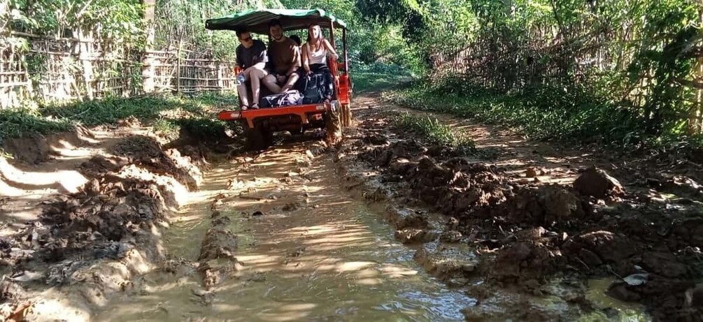 A vehicle navigating a muddy, waterlogged path in a forested area. 2