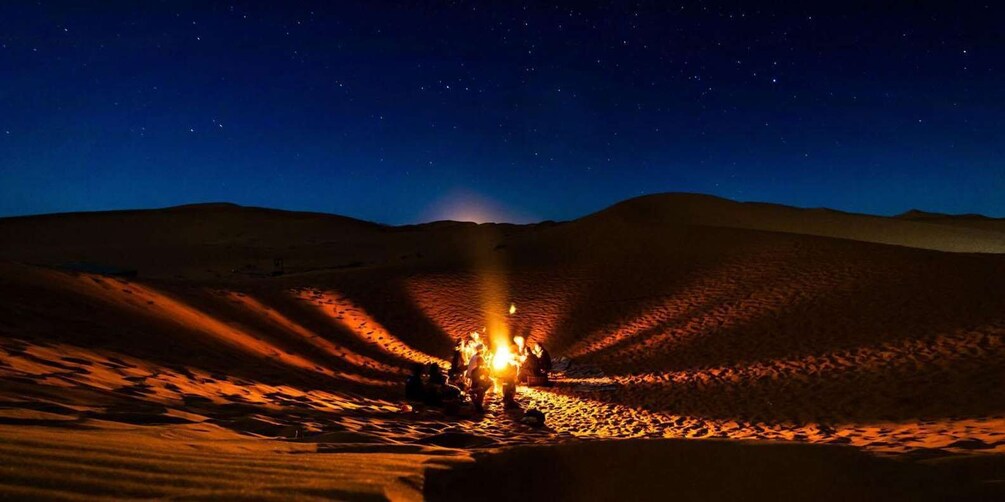 A desert at night with a campfire and a vehicle in the foreground. 1