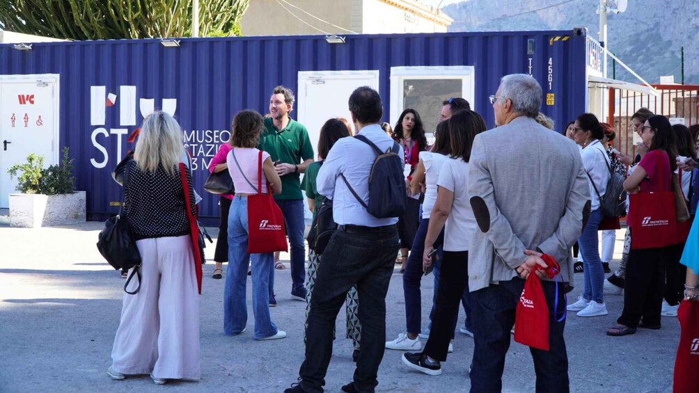 A group of people standing in front of a blue container with 'MUSEO STAZIONE 3' written on it. 3