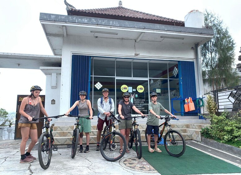 A group of people with bicycles in front of a building with a blue door and windows. 4
