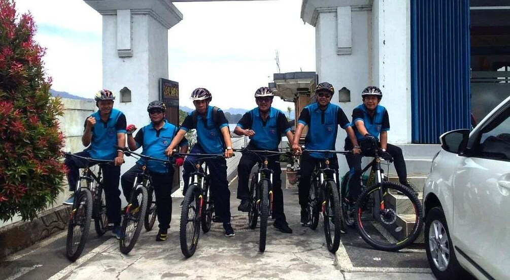 A group of cyclists in blue jerseys lined up in front of a building with a white door and a blue awning. 2