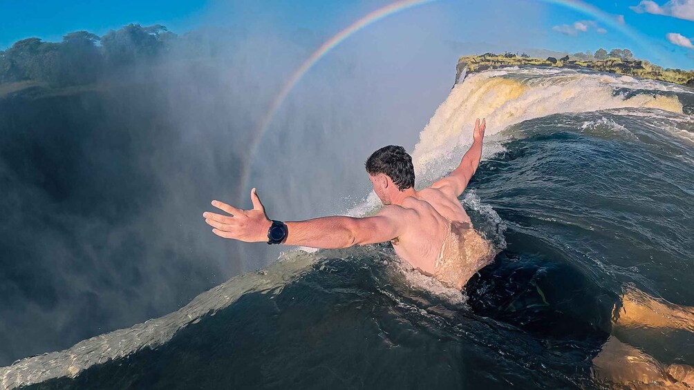 A person surfing a wave with a rainbow in the background. 1