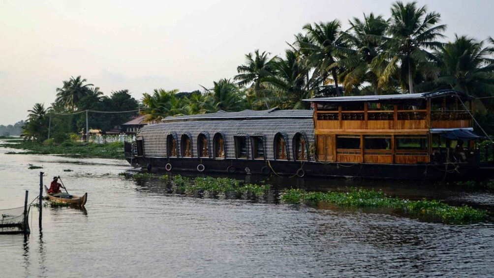 A houseboat with a wooden upper deck and a person rowing a small boat nearby. 4