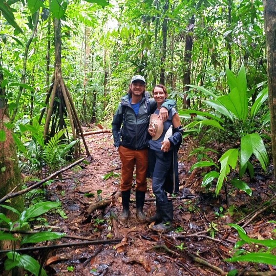 Three people in a forested area with dense vegetation and a muddy ground. 3